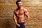 Muscle shaped man posing on gym brick wall