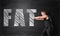 Muscled young man pushing big drawn fat word by both hands on the background of a blackboard