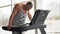 Muscular athletic bodybuilder fitness model running treadmill gym near big window