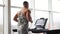 Muscular athletic bodybuilder fitness model running treadmill gym near big window