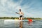 Muscular athletic man in sunglasses actively rowing with an oar sitting on a sup board, swims on a pond. Summer fun on the water