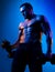 Muscular bodybuilder guy doing exercises with dumbbells  on blue neon. Naked athlete with strong body. Shirtless