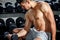 Muscular bodybuilder guy doing exercises sitting with weight lifting dumbbells in gym . Shirtless sport young fitness man training