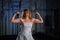 A muscular bride in a wedding dress poses in front of the camera in the gym and shows her big biceps