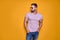 Muscular confident bearded male in shirt, jeans and stylish sunglasses standing in studio over yellow background