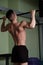 A muscular guy with a naked torso pulls himself up on the horizontal bar in the gym, a shot from the back.