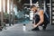 Muscular guy tying sneakers laces at gym, empty space