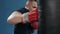 Muscular handsome fighter giving a forceful forward kick during a practise round with a boxing bag, kickboxing. Close up