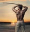 Muscular handsome guy with sword at sunset