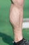 Muscular leg with vein at stadium or arena on sunny outdoor. Foot in black sport fashion shoe on green grass. Health and healthy l