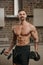 A muscular man with a beard is posing with dumbbells in his apartment