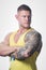 Muscular man with blue eyes and tattoo in the yellow tank top looking away on the white background in a gym