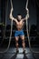 Muscular man bodybuilder training with ropes in the gym and posing. Fit muscle guy workout with weights and barbell