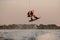 muscular man holds cable and masterfully jumping above splashing wave on wakeboard.