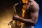 Muscular man with naked torso playing on saxophone with smoked colorful background