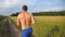 Muscular man running at country road. Young athletic guy jogging at rural trail over the field. Male sportsman training