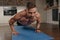 A muscular man with tattoos is doing pushups on a blue yoga mat in his apartment