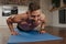 A muscular man with tattoos is doing pushups on a blue yoga mat in his apartment