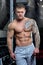 Muscular shirtless shredded strong relaxed man with blue eyes and tattoo poses in a gray pants in a gym