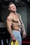 Muscular shirtless strong man with blue eyes and tattoo poses with smile in a gray pants in a gym