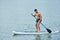 Muscular sportsman swimming on sup board in city lake, keeping long oar.