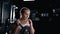 A muscular sportswoman is doing exercises in the dark gym. Self confident girl is engaging with barbell. Crossfit