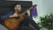 Music composer writing a song at home sitting on his bed holding an acoustic guitar. Music concept