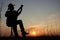 Music concept of black silhouette of man with western hat cowboy and instrument with grass at sunset or sunrise. Musician play