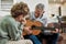 Music time. Mature caucasian man grandfather playing guitar to his little grandson, teaching new musical instrument