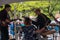 Musical group is seen from the back as they play their instruments in front of a crowd at an outdoor fair. There is a woman