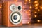 Musical speaker close-up on a wooden background. Glowing garlands in the background