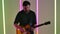 Musician playing on electric guitar against the background of multicolored neon lamps in the studio. Rock, ska punk