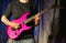 Musician playing pink electric guitar on stage.