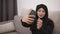 Muslim beautiful woman in black hijab taking a selfie with her mobile phone, closing her face with a scarf. Lady is