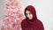 Muslim caucasian lady in hijab is standing on Christmas tree background and looking at camera