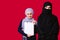 Muslim girls on a red background. A young girl holds a folder, white sheet, smiles and looks at the camera, another