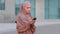 Muslim islamic girl woman in hijab stands on street outdoors city uses mobile phone looks at smartphone screen cellphone