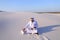 Muslim male architect sitting with laptop on sand in desert on h