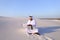 Muslim male architect sitting with laptop on sand in desert on h