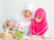 Muslim mother point to vegetable salad while little girl with pink hijab has fun with mixing salad put on the table