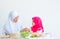 Muslim mother serve glass of milk to her little girl and also look to each other with smiling, bowl of vegetable salad on the