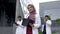Muslim pleasant doctor in hijab, standing outdoors in front of hospital, with team behind