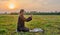 A Muslim senior man wearing a skullcap and traditional clothes prays at sunset