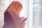 Muslim woman with hijab praying indoor at bright window
