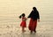 Muslim woman with little girl walking on beach