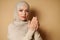 Muslim woman wearing beige hijab and traditional clothes praying namaz, on beige background with copy space