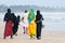 Muslim women walk along the beach, a man walks ahead