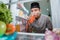 muslim young man cheating and drinking a a glass of water or juice in the fridge while fasting