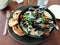 Mussels dish served with a fresh salad, chili pepper and toasted white bread on gray plate in restaurant