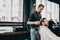 Mustachioed barber dressed in a black shirt with a red bow tie makes a stylish hairstyle to young man in a barbershop